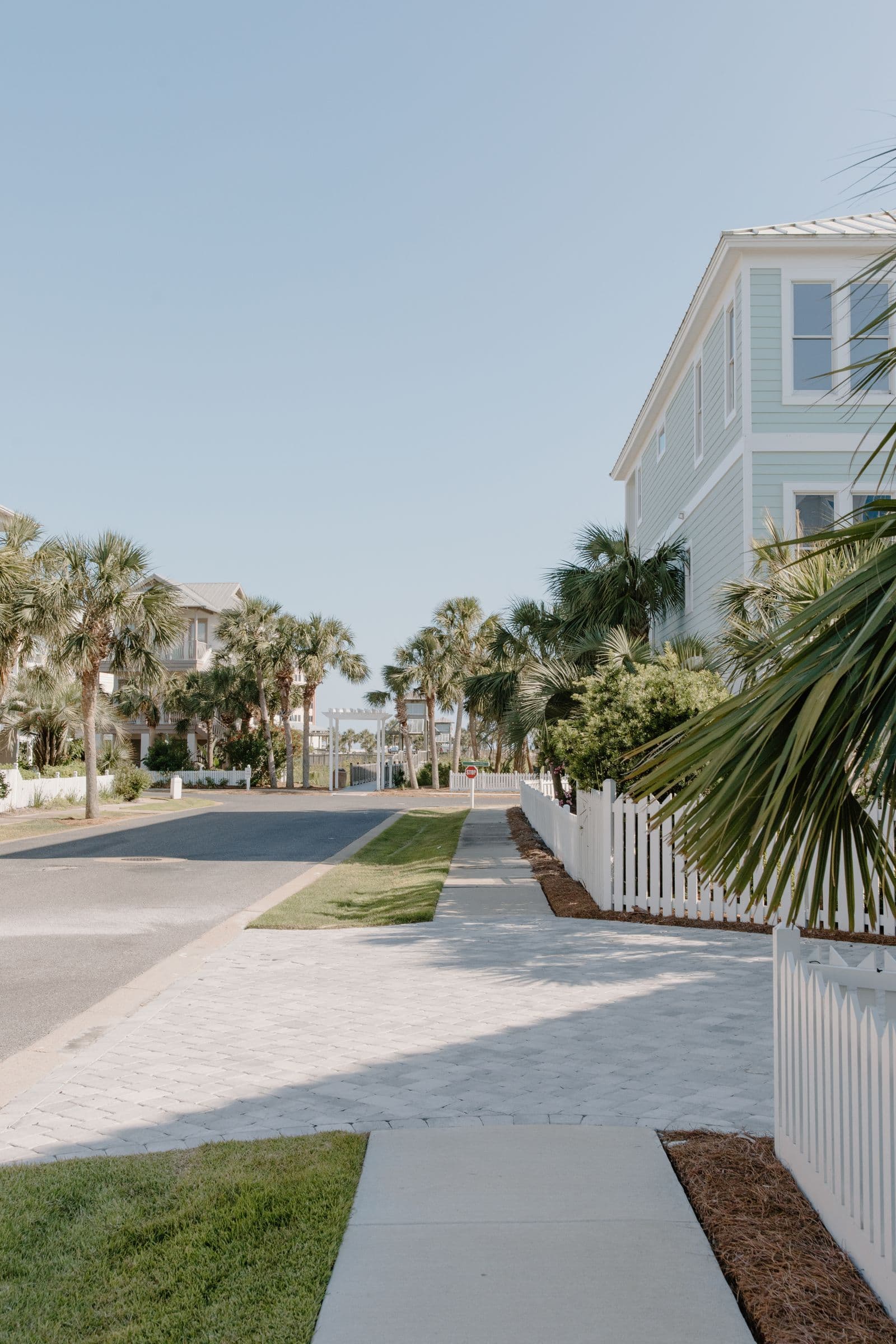Bright planned-community street with pavers, palms, and white picket fencing