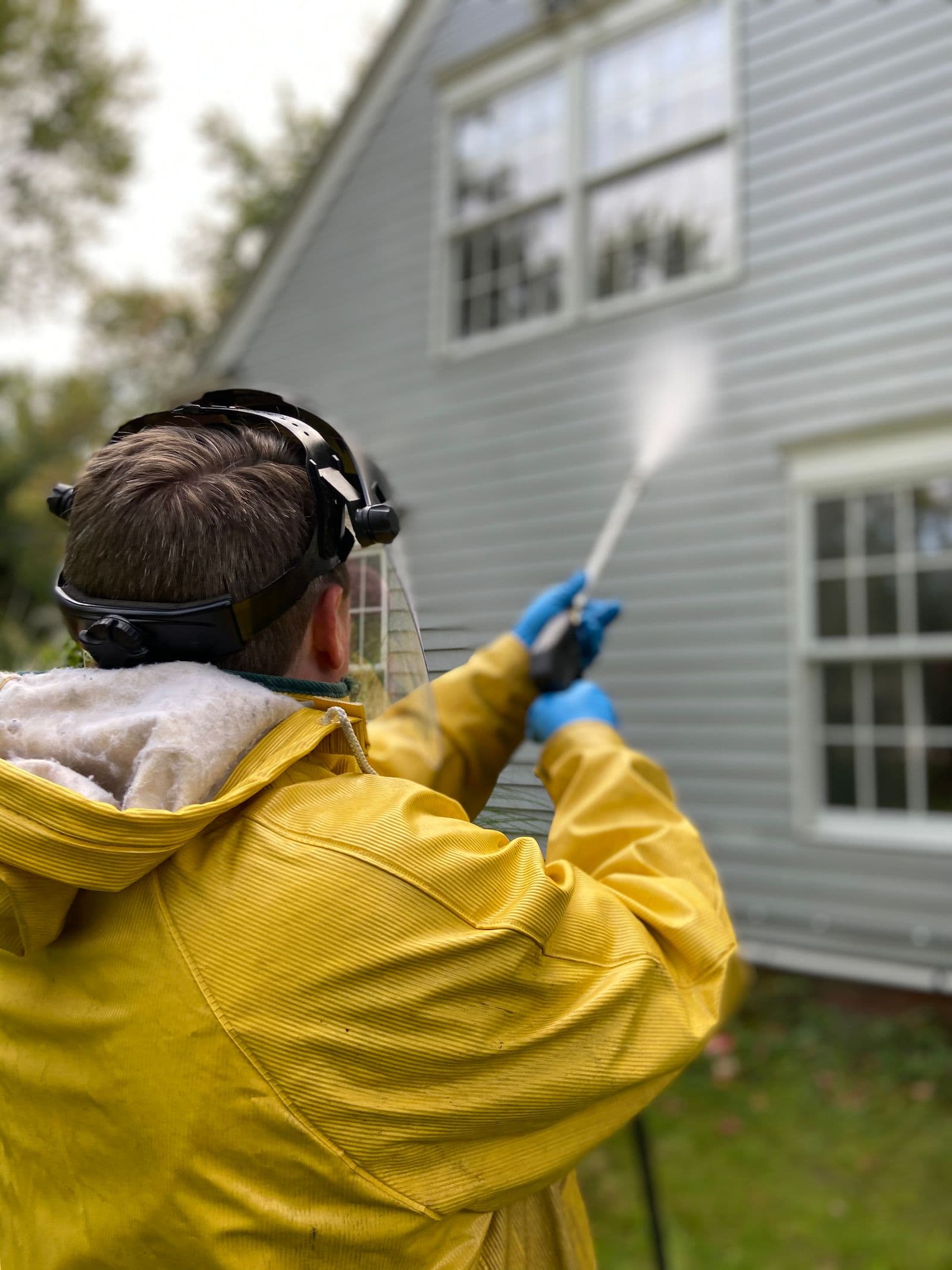 Technician in protective gear soft washing home siding